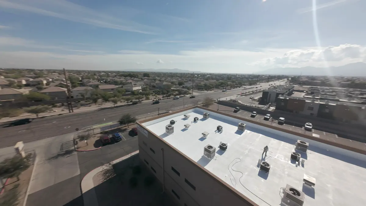 Aerial view of a white-coated commercial flat roof with rooftop HVAC units and a roofer working on the roof