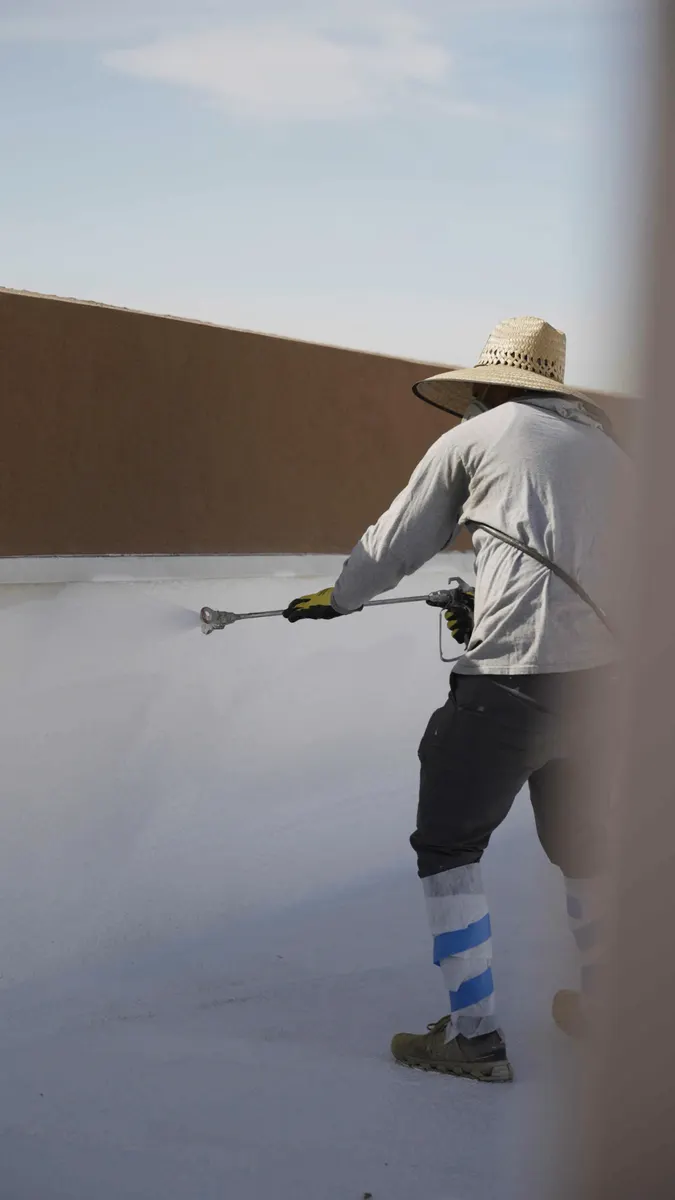 Simply Roofing roofer in a sun hat spraying white coating on a commercial flat roof