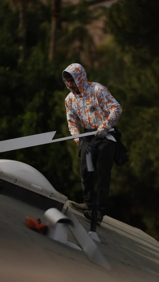 Roofer carrying a length of metal flashing across a low-slope roof