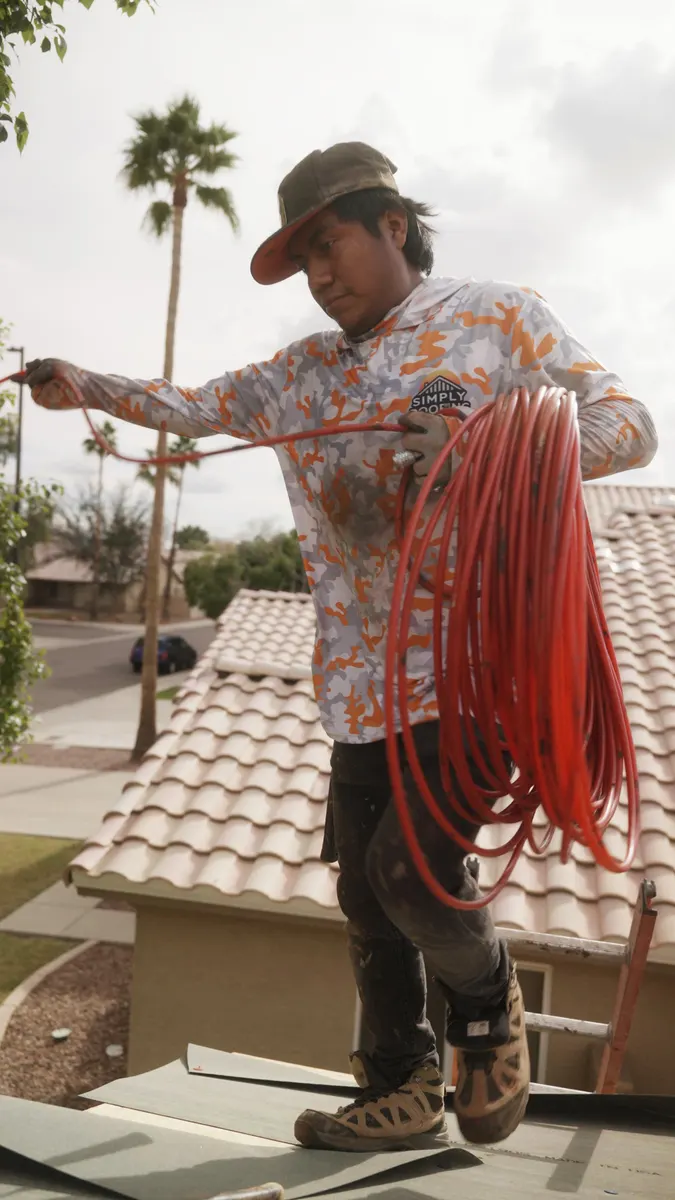 Roofer coiling an air hose on a tile roof