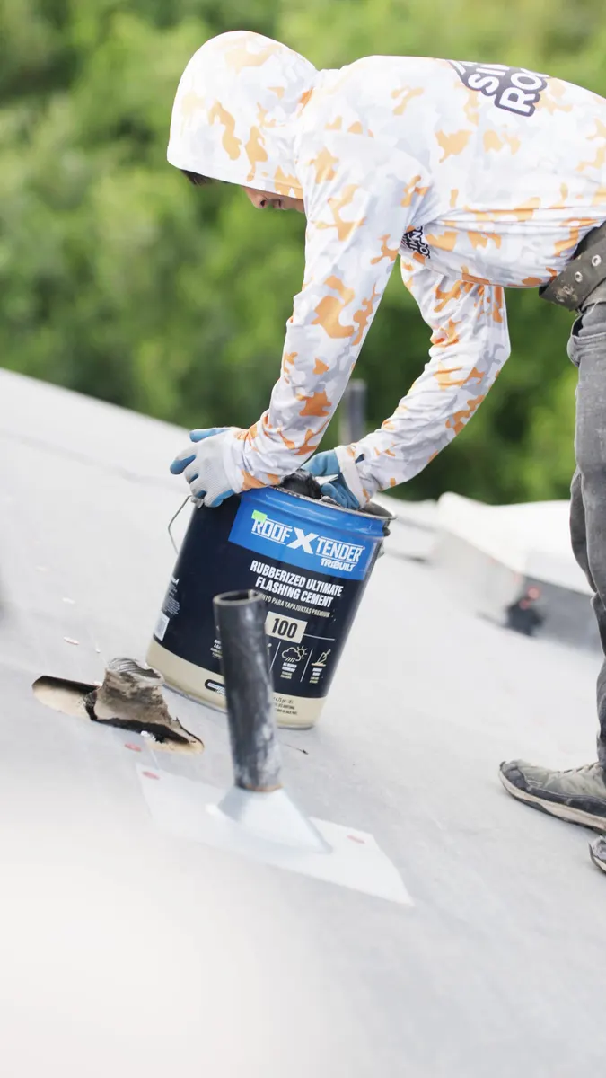 Roofer opening a bucket of flashing cement beside a new pipe flashing