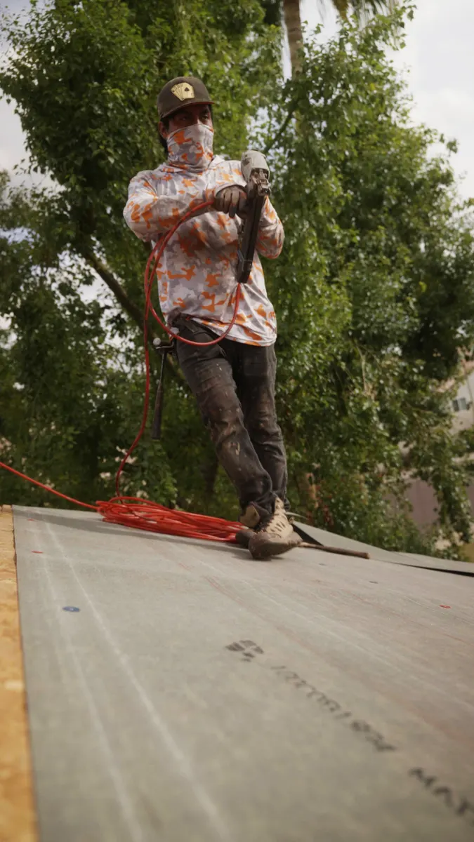 Roofer with a pneumatic nailer and air hose standing on new roof underlayment
