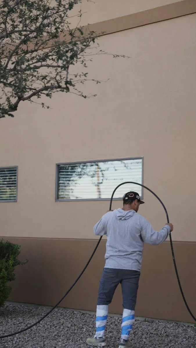 Roofer pulling a spray hose along the side of a commercial building