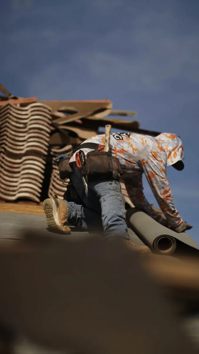 Roofer rolling out underlayment next to stacked roof tiles