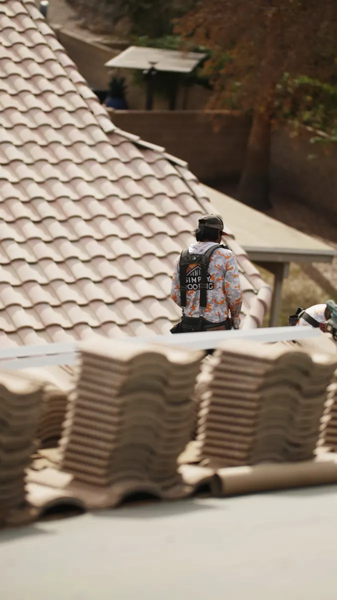 Simply Roofing crew member on a tile roof behind stacks of lifted roof tiles