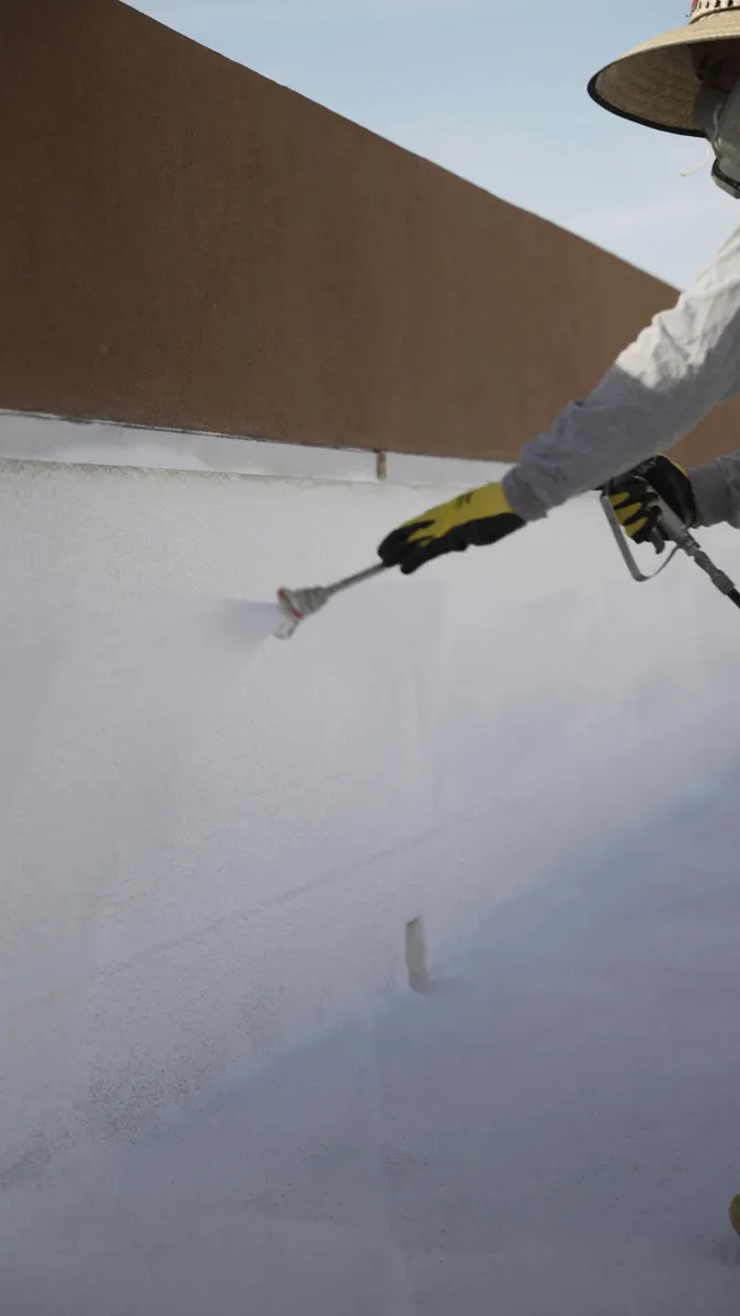 Close-up of a roofer spraying white coating onto a parapet wall