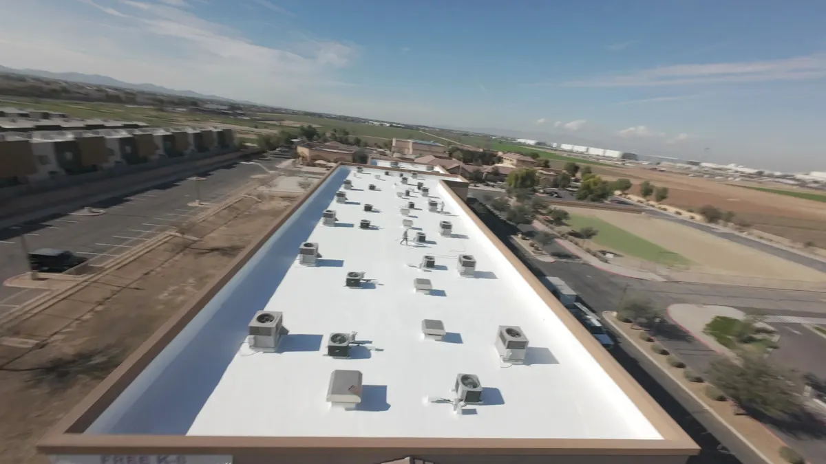 Aerial view of a long commercial building with a white flat-roof coating and rows of rooftop HVAC units